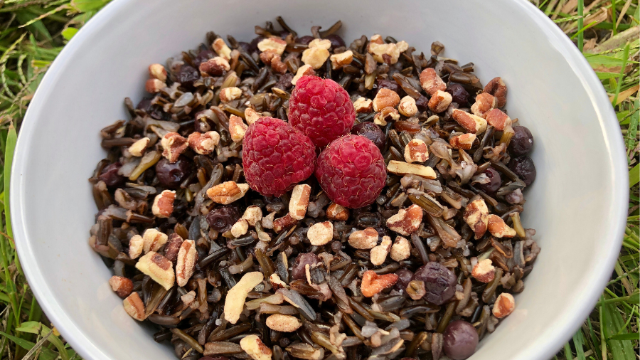 a bowl of wild rice with blueberries, topped with pecans and raspberries