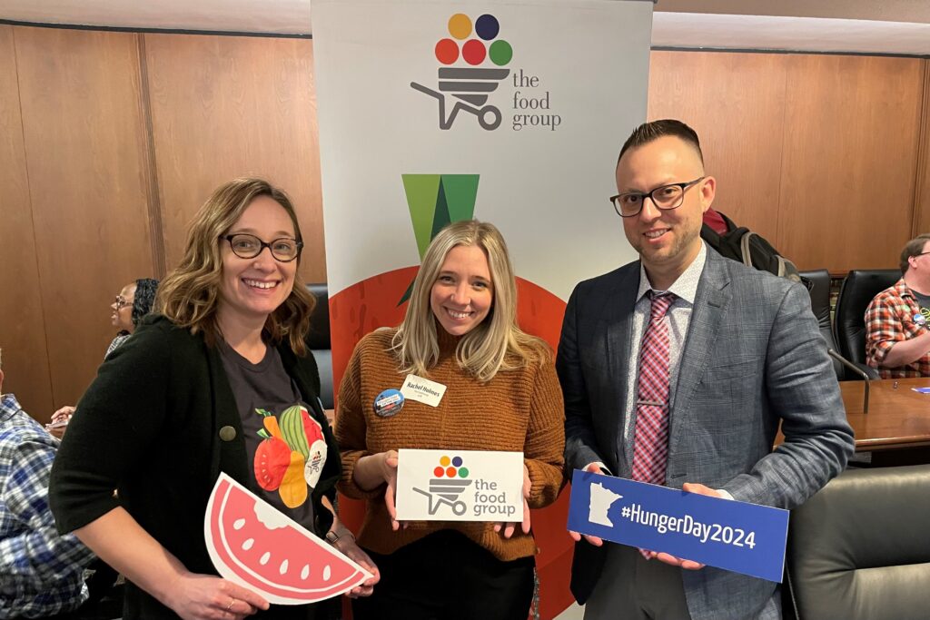 Two women and a man standing in front of a banner reading The Food Group.