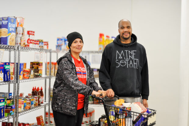 Two people shopping the food shelf with a cart of groceries