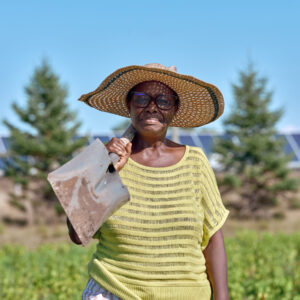 A woman with a shovel stands smiling with a shovel in her field at our agrisolar farm