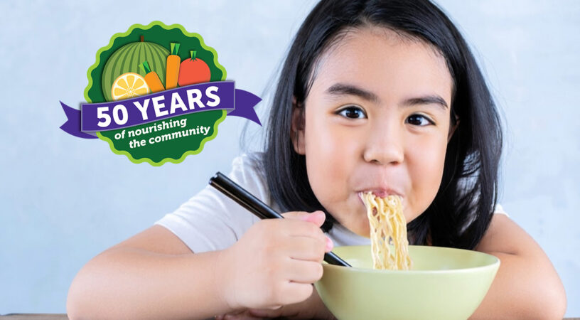 Girl eating noodle. Also showing The Food Group's 50th year seal.